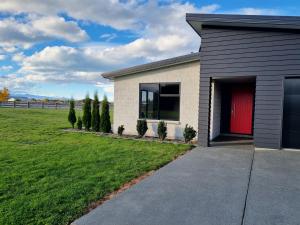 a house with a red door and a green field at Ben Ohau Views On The Drive in Twizel