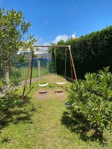 a swing set in a yard with a hedge at La Fleur des Marais - Maison tout confort au calme, grand jardin & balançoire in Le Château-dʼOléron