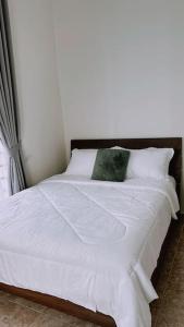 ein Bett mit weißer Bettwäsche und einem grünen Kissen darauf in der Unterkunft Kamilia Homestay KB City Centre in Kota Bharu