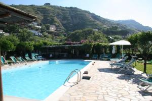 a large swimming pool with chairs and an umbrella at Tenuta Villa Tara in Ischia