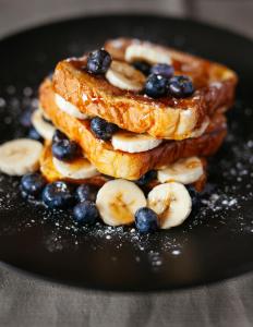 a stack of pancakes with bananas and blueberries on a plate at Hotel LA CASA DELHI AIRPORT in New Delhi