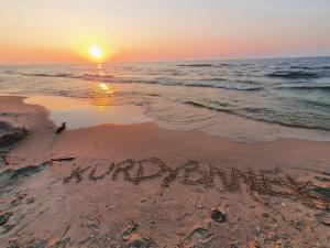 una puesta de sol en la playa con el wordiversary escrito en la arena en Kurdybanek - Domki letniskowe en Stegna