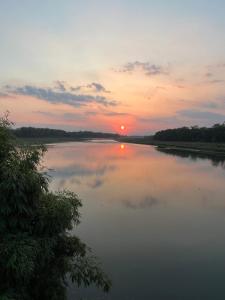 a sunset over a river with the sun setting at Chitwan Park Village in Sauraha