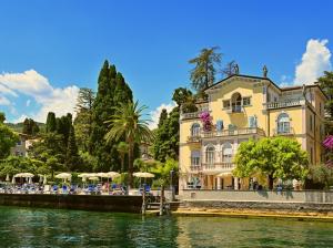 un bâtiment avec des chaises et des parasols à côté d'une rivière dans l'établissement Hotel Monte Baldo e Villa Acquarone, à Gardone Riviera