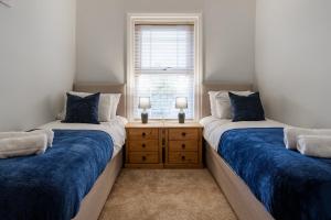 a bedroom with two beds with blue sheets and a window at Wrea Cottage, 2 Bedrooms WiFi & Parking near Ribby Hall in Wrea Green