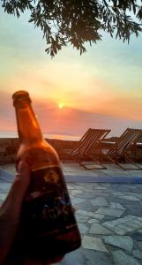 a person holding a bottle with the sunset in the background at Aegean living Villa in Agios Romanos