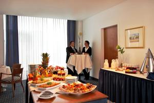 two people standing in a room with a table with food at H4 Hotel Kassel City, Trademark Collection by Wyndham in Kassel