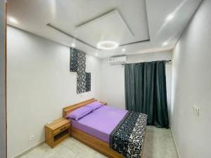 1 dormitorio con cama morada y ventana en Appartement meublé 2chambres 1salon T3 N10 Résidence LES 11 PLURIELLES, en Lomé