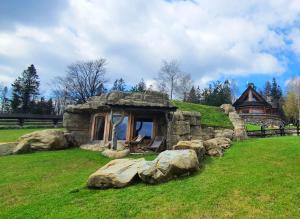 a small stone house in a field with rocks at Osada Jaworzyny - Domek Hobbita z jaskinią SPA in Tokarnia