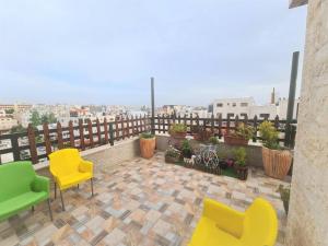 Khalda Rooftop Apt. في عمّان: بلكونه فيها كراسي صفراء و خضراء على مبنى