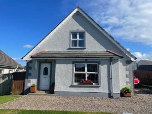 a grey house with a window and flowers in a driveway at Wind Rose Rooms in Ballycastle