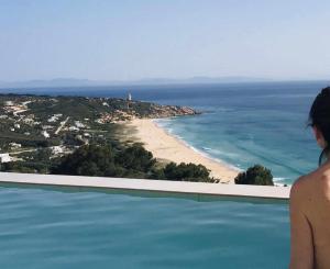 a woman standing on the edge of a swimming pool overlooking a beach at Villa El Buzo in Zahara de los Atunes