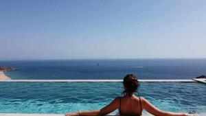a woman sitting on the edge of a pool looking out at the ocean at Villa El Buzo in Zahara de los Atunes