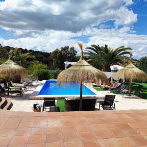 un complejo con una piscina con sombrillas de paja en Casa Rural El Canto Del Agua, en Malpartida de Plasencia