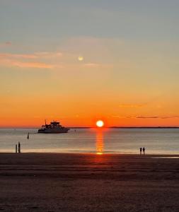 a boat in the ocean at sunset with people on the beach at Haus Andersen Apartment ZWEI in Norderney