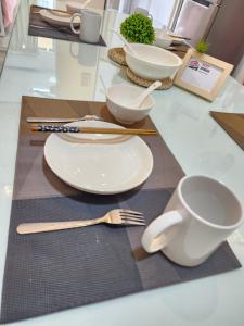 Ixora Coliving Lifestyle Homestay في آير كيروه: طاولة عليها صحون وادوات بيضاء