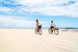 two people riding bikes on the beach at Pousada Marceneiro in São Miguel dos Milagres
