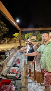 Dois homens estão ao lado de um grelhador. em Bodrum Masali Camping em Muğla