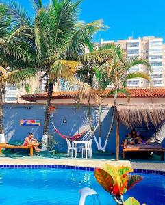 a swimming pool with palm trees and people sitting on chairs at Hostel Praia Centro Itanhaém in Itanhaém