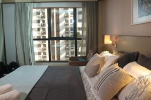 ブラジリアにあるFlat Premium Particular Cullinan Hotelのベッドと大きな窓が備わるホテルルームです。