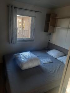 a bedroom with a bed with two pillows and a window at Mobil-home premium 325 in Narbonne