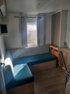 een kleine kamer met een blauwe bank en een raam bij Mobil-home premium 325 in Narbonne