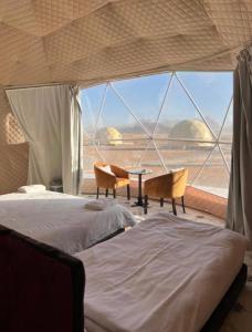 a room with a bed and chairs and a large window at Star Guide Camp in Wadi Rum