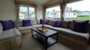 a living room with a couch with purple pillows and a table at 3 Bedroom Stylish Caravan - Vans With Business Sign Not Allowed in Port Seton