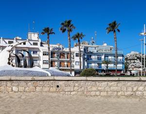 a large white building with palm trees in the background at Hotel Rio Mar in Peniscola