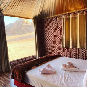 Bett in einem Zimmer mit einem großen Fenster in der Unterkunft Areen camp, Wadi Rum in Wadi Rum
