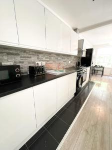 Immaculate 1 bedroom apartment in Orpington في أوربنغتون: مطبخ بدولاب أبيض وقمة كونتر أسود