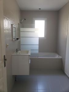 a white bathroom with a tub and a sink and a window at Chambres in Yvré-le-Pôlin