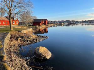 a lake with a red house and a tree and a rock at Captivating Harbor View Suite in Östhammar