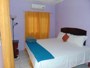 Schlafzimmer mit einem Bett mit weißer Bettwäsche und orangefarbenen Vorhängen in der Unterkunft Tropical Manor Inn - Kingston in Kingston