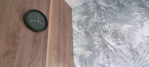 une horloge sur un mur en bois avec du papier peint de palmier dans l'établissement 62m2 Apartament PREMIUM Łąki i Pola, ELEKTRYCZNE ROLETY, KLIMATYZACJA, GARAŻ, ŁADOWARKA AUT ELEKTRYCZNYCH, à Suwałki