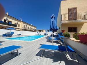 a swimming pool with blue lounge chairs and an umbrella at Blue Coral in San Vito lo Capo