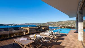 un balcon avec des tables et des chaises ainsi qu'une piscine dans l'établissement Villa Ramarin III with infinity heated pool, jacuzzi and sauna by the sea in Rogoznica, à Rogoznica