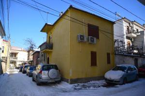 a yellow building with cars parked on a snow covered street at Piro's Cozy Rooms - City Centre in Korçë