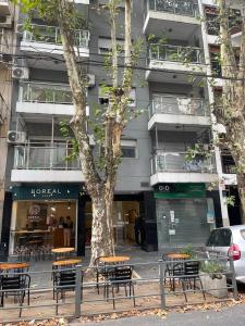 ブエノスアイレスにあるDepartamento 2 amb Villa Urquizaのテーブルと椅子が並ぶ建物の前の木