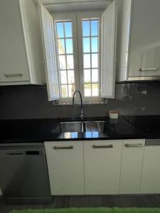 uma cozinha com armários brancos, um lavatório e duas janelas em Casa da Celeste em Maljoga de Proença