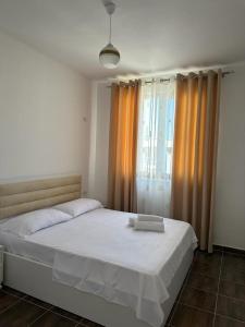a bedroom with a bed with white sheets and orange curtains at Marjana's Apartment 3 in Lezhë
