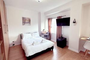 a bedroom with a bed with white sheets and a television at Charming Studio Flat with Private Patio Balcony in the Heart of Chelsea in London