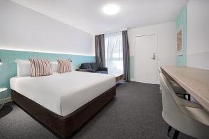 ein Hotelzimmer mit einem großen Bett und einem Schreibtisch in der Unterkunft Gosford Palms Motor Inn in Gosford