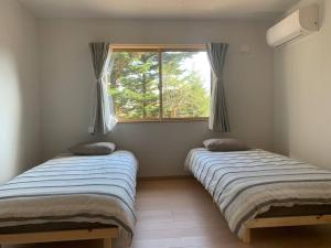 two beds in a room with a window at 木漏れ日ハウス in Karuizawa