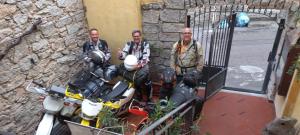 three men standing in front of a gate with a motorcycle at b&b il Portico Orgosolo in Orgosolo