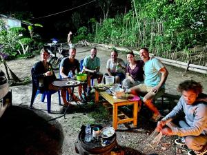 a group of people sitting around a table next to a fire at Santiago Bed and Breakfast at Desa Wisata Moni in Kelimutu