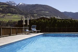 a swimming pool with two chairs and umbrellas in front of mountains at Pension Kleon in Rifiano