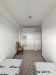 Cette chambre comprend 2 lits et une chaise. dans l'établissement RESIDENCE CENTRO COMMERCIALE - WALTERIGATO Apartments SOLO PER FAMIGLIE, à Lido di Jesolo