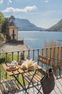 a table with an open book on a balcony with a lake at Deriva Apartment on Careno's Beach by Rent All Como in Nesso
