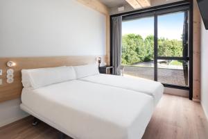 un letto bianco in una stanza con una grande finestra di B&B HOTEL Guimarães a Guimarães